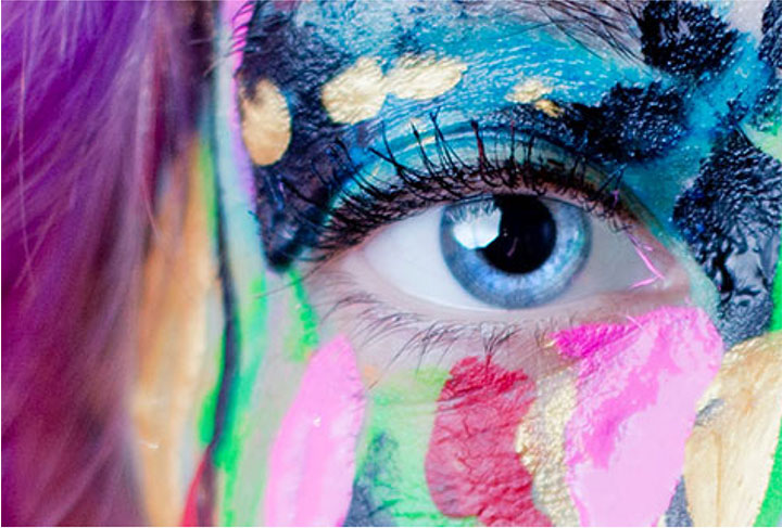 Close up on an eye. The surrounding face is covering in colourful paint